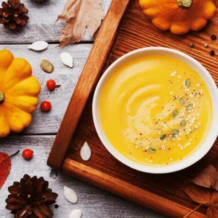 pomarańczowa zupa krem w białej misce stojącej na drewnianej desce wśród jesiennych dekoracji - tytułowa.